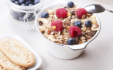Breakfast cereal with raspberries and blueberries next to plate with cookies.