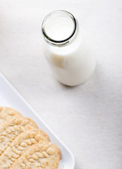 Milk bottle next to plate with cookies. Vertical studio shot.