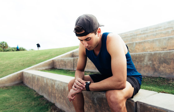 Young man wearing sports clothing, sitting on step, looking at activity tracker, South Point Park, Miami Beach, Florida, USA