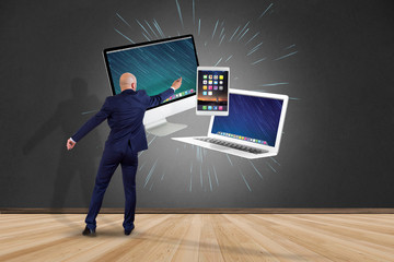 Businessman in front of a wall with Computer and devices displayed on a futuristic interface - Multimedia and technology concept