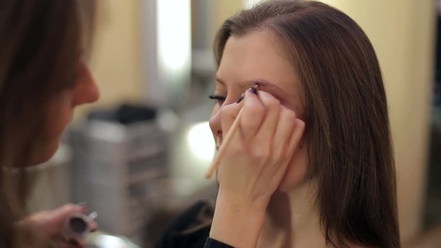 Makeup artist making professional makeup for young woman in beauty studio.