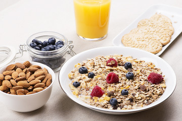 Cereal bowl breakfast with milk, raspberries and blueberries next to orange juice, cookies and container with almonds....