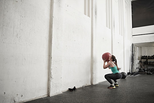 Woman throwing fitness ball against wall in cross training gym