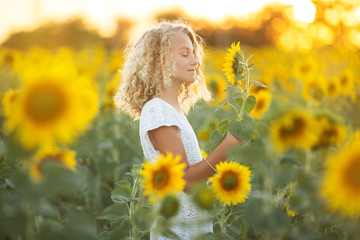 Fototapeta na wymiar Pretty curly girl in white dress in field of sunflowers over sunset lights