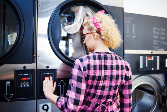 Woman pressing washing machine buttons at laundrette