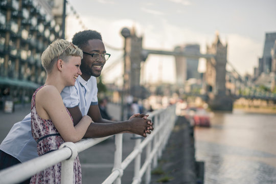 Young couple outdoors, leaning on railings beside river, smiling