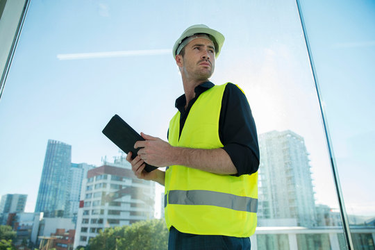 Man wearing hard hat and hi vis vest, holding digital tablet
