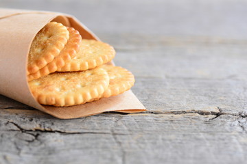 Dry wheat cookies in a wrapping paper and an old wooden background with empty copy space for text. Salty crackers cookies idea for kids or adults. Rustic style