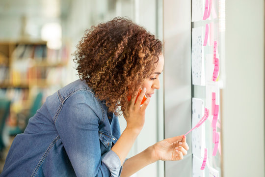 Female digital designer making phone call and looking at adhesive notes on office wall
