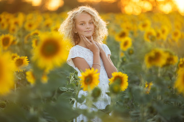 Naklejka na ściany i meble Happy pretty girl in white dress having fun in field of yellow sunflowers