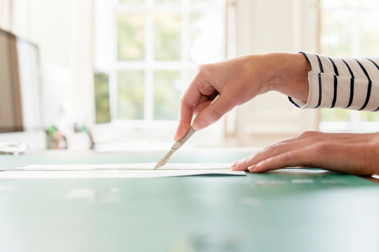Hand of female designer cutting paper with scalpel in creative studio