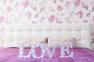 LOVE letters with light bulbs in glamour pink bedroom interior with stylish bed