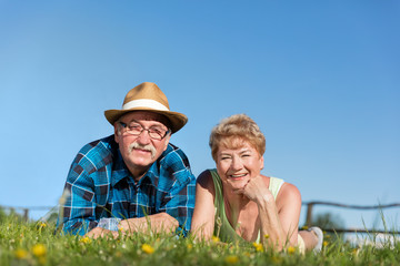 Senior couple lying on the summer field in green grass