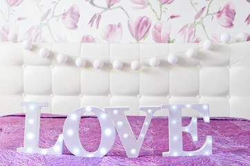 LOVE letters with light bulbs and white cotton light balls string in glamour pink bedroom interior with stylish bed and pillows