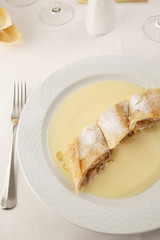 Apple pie slice with vanilla mousse arranged on a plate, Wineglass in background, Traditional dessert in elegant setting, Selective focus with soft light
