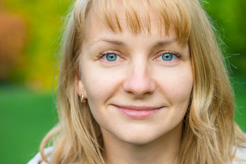 Portrait of attractive smiling caucasian young woman in spring park looking at camera - close up.