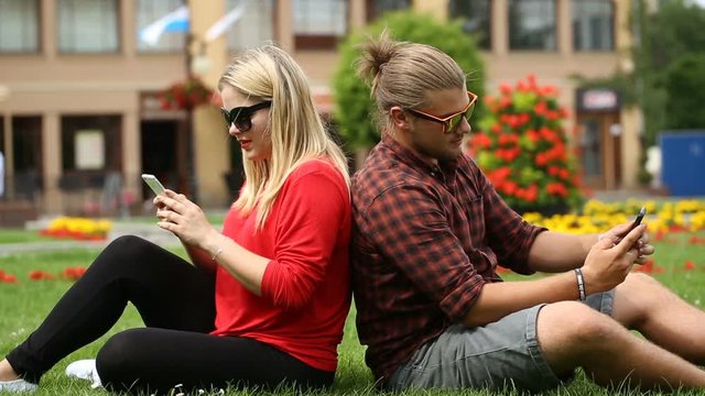 Happy couple sitting on the grass and doing photos on smartphone
