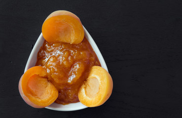 Apricot jam and apricots on black wooden background
