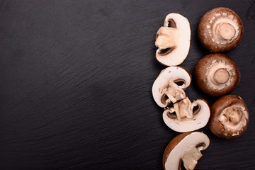 Gray mushrooms champignons whole and sliced lie on a stone black slate board, background