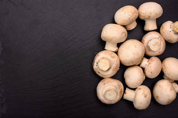 Whole mushrooms champignons whole lie on a black stone slate, background