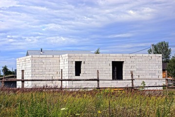 Fototapeta na wymiar строительство белого кирпичного дома за забором возле поля с травой 