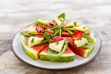 Delicious watermelon pizza with cheese and herbs on a wooden table.
