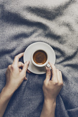 Woman hands holding tasty coffee espresso in small cup on grey plaid. Home concept. Top View.