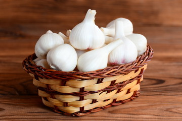 Fresh garlic in a wicker basket isolated on a wooden background. Young garlic harvest concept. Closeup