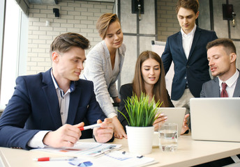 Brainstorm. Group of business people looking at the laptop together. One business woman looking at camera.