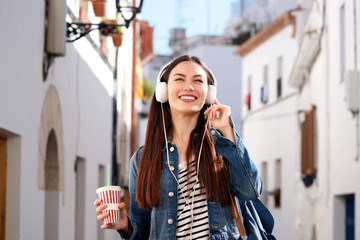 Fototapeta premium Woman walking on city street with drink and headphones
