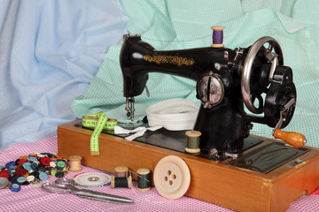 An old, hand sewing machine with a needle, retro coils with colored threads, bright buttons and pieces of colored cotton fabric.