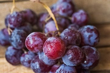 Blue grapes lie on a wooden background. Grapes macro. Grapes with droplets of water. Grapes in a cut. Grapes and wine corks. Blue and green grapes