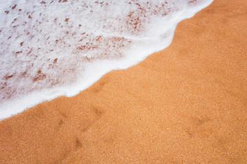 full frame shot of a smooth foamy wave covering the sand