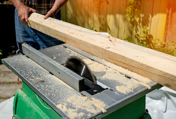 Male hand cuts with a circular saw a piece of Board on a Sunny day, close-up. Toned.