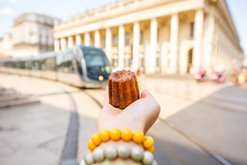 Holding a traditional Bordeaux sweet cake called Canele outdoors on the street near the Grand theatre building in Bordeaux © rh2010