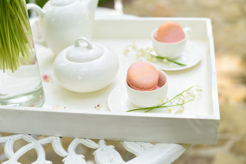White tray with a teapot and with macaroons in cups on a forged table