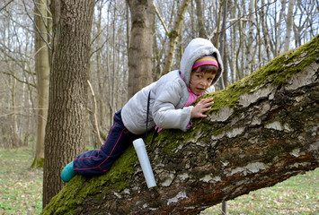 The little girl creeps on a trunk of a big tree in the spring wood