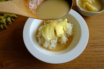 Pouring coconut milk on the sticky rice toping with durian on the wooden table