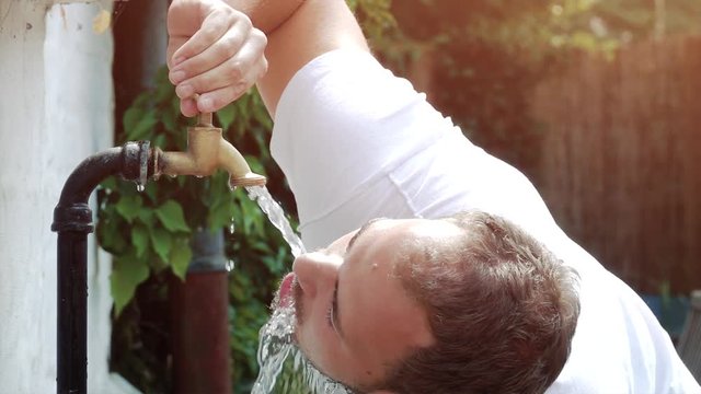 super slow motion shot of faucet, young man drinking fresh water dripping and splash on a hot summer day