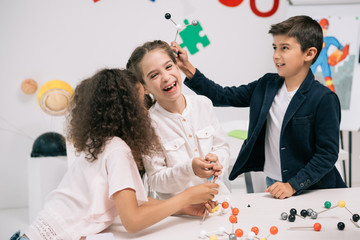 Multiethnic schoolchildren working with molecular model and smiling in class