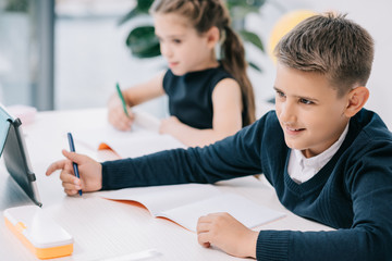 Schoolchildren writing in blank exercise books while studying at desk in classroom
