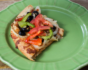 Closeup on vegetarian pizza with tomatoes, black olives, mushrooms, onions, green peppers and mozzarella, on green plate, against wooden background 