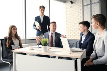 Brainstorm. Group of business people looking at the laptop together. One business woman looking at camera.