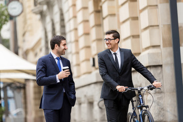 Two young businessmen with a bike in city centre