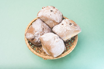 Homemade muffins with raisins and powdered sugar in a wicker basket against a light mint color
