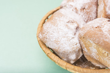 Homemade muffins with raisins and sugar powder in a wicker basket against a light mint color, on the right side of the frame