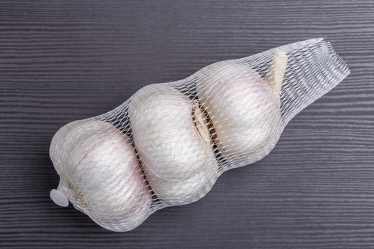 Packaged white garlic bulbs in net place on wooden table, general and useful seasoning for tasty foods.