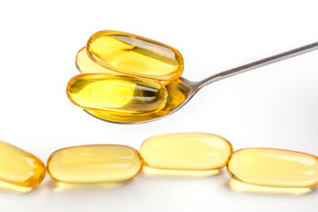Golden soft gel capsules served by spoon and blurred another capsules in background, optimal oil supplement intake concept.