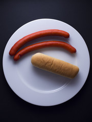Two red sausages from Denmark made from pork meat served on white plate with bread, ketchup and mustard sauce. Isolated on black background 