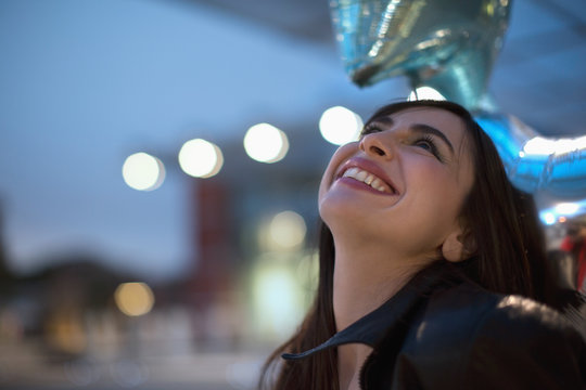 Beautiful young woman with shiny star balloons going out in the evening smiling
